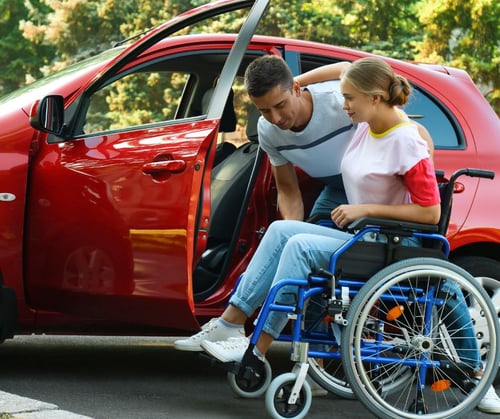 Persoonlijke assistent helpt een jonge vrouw met een handicap bij het instappen van de auto.